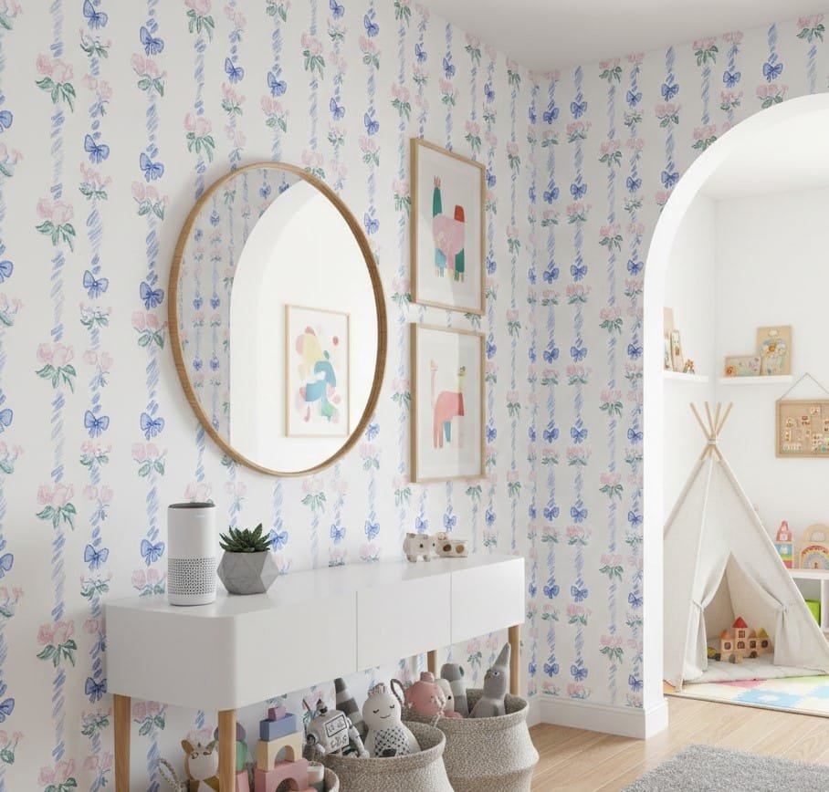 Light-filled playroom styled with pastel ribbon and rose wallpaper, white storage console, round mirror, and soft toy baskets.