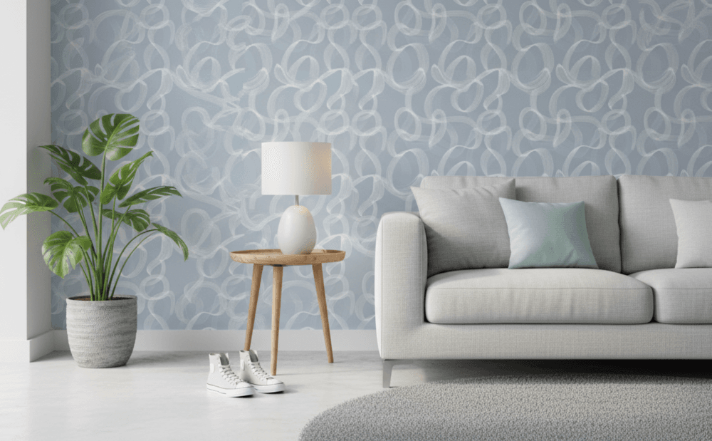 Soft blue abstract wallpaper with flowing white brushstroke loops in a modern living room with a light grey sofa, side table, lamp, and indoor plant.