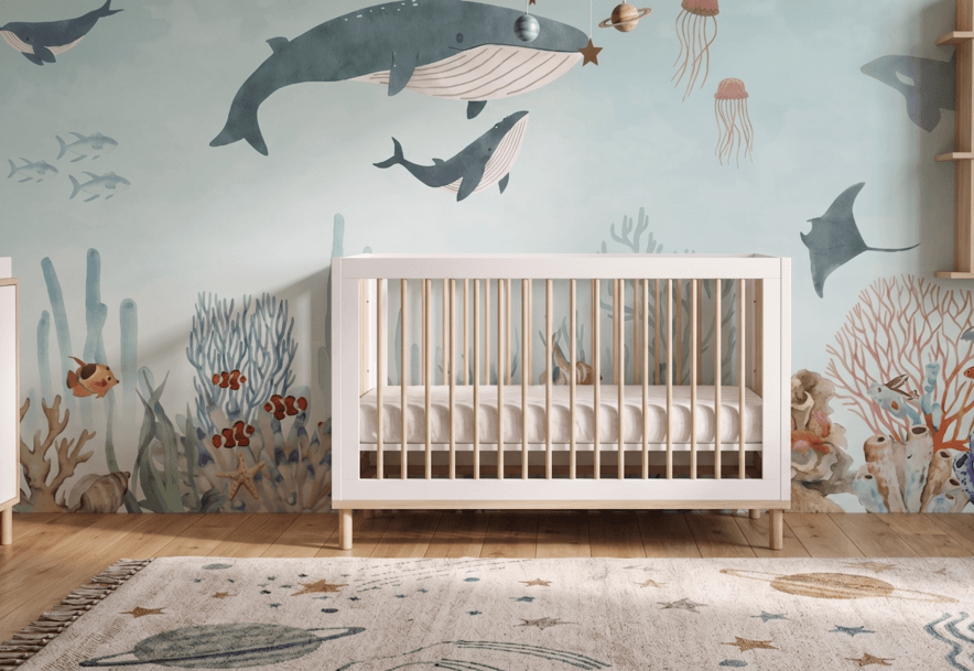 A nursery featuring the Ocean Wonders Mural with whales and underwater sea life behind a white crib.