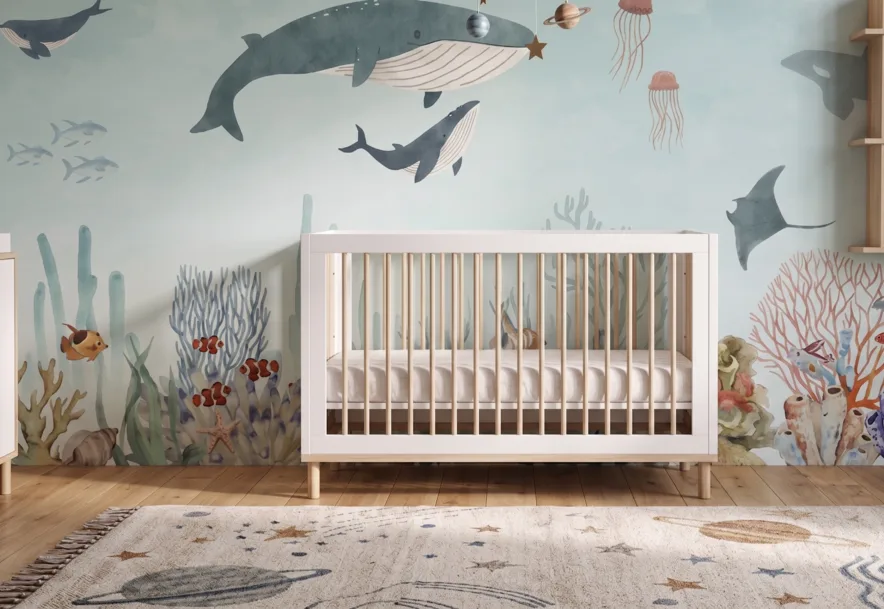 A nursery featuring the Ocean Wonders Mural with whales and underwater sea life behind a white crib.